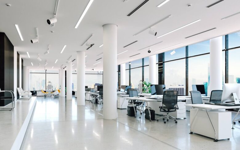 ufficio open space luminoso con scrivanie bianche, collone bianche e vetrate